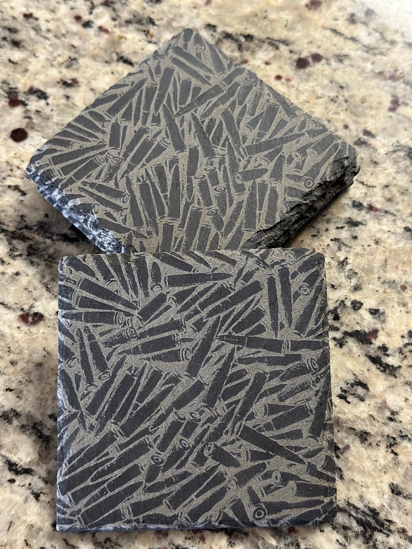 Engraved slate coasters with pile of bullets on a dark slate background.