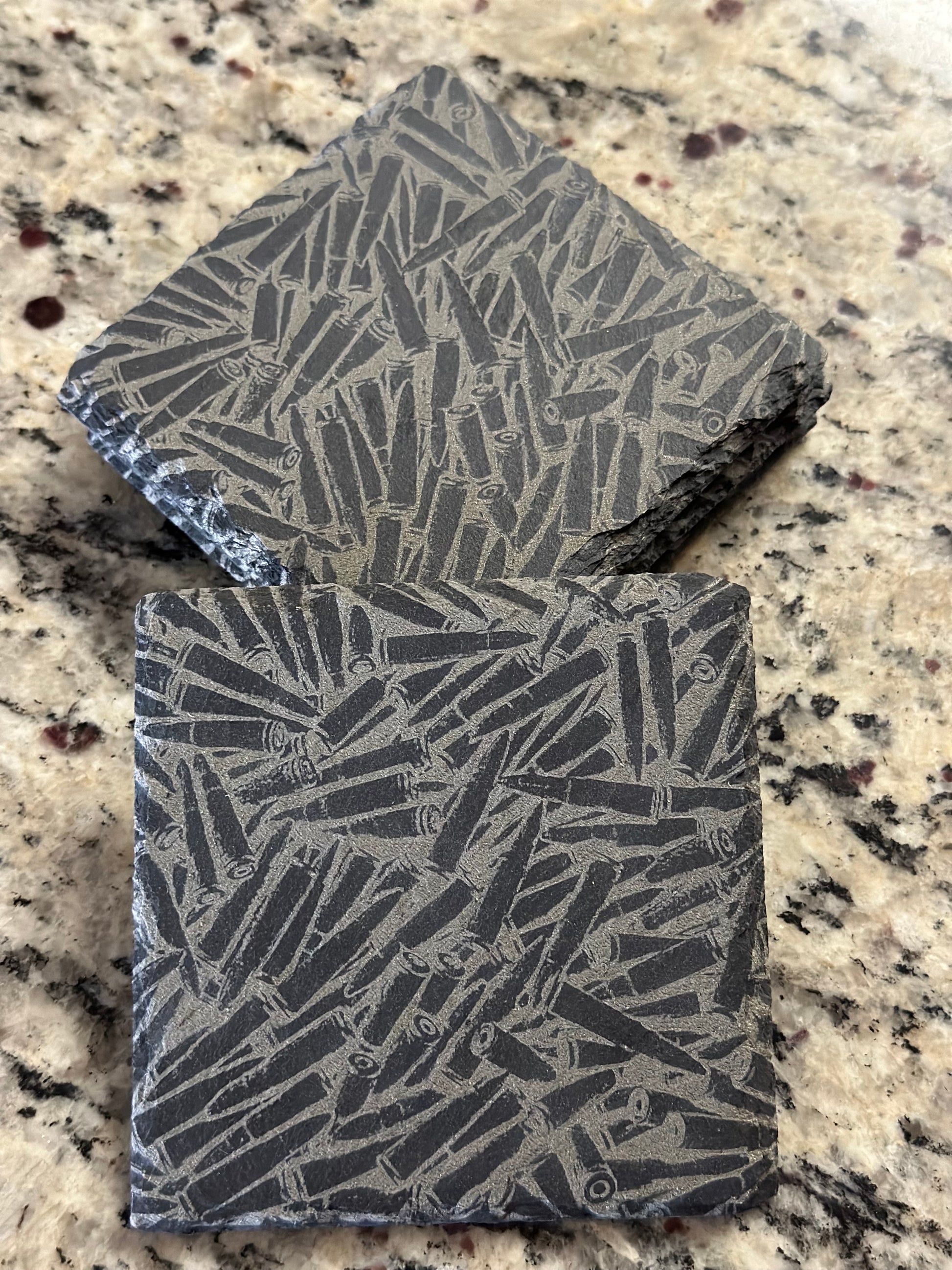 Engraved slate coasters with pile of bullets on a dark slate background.