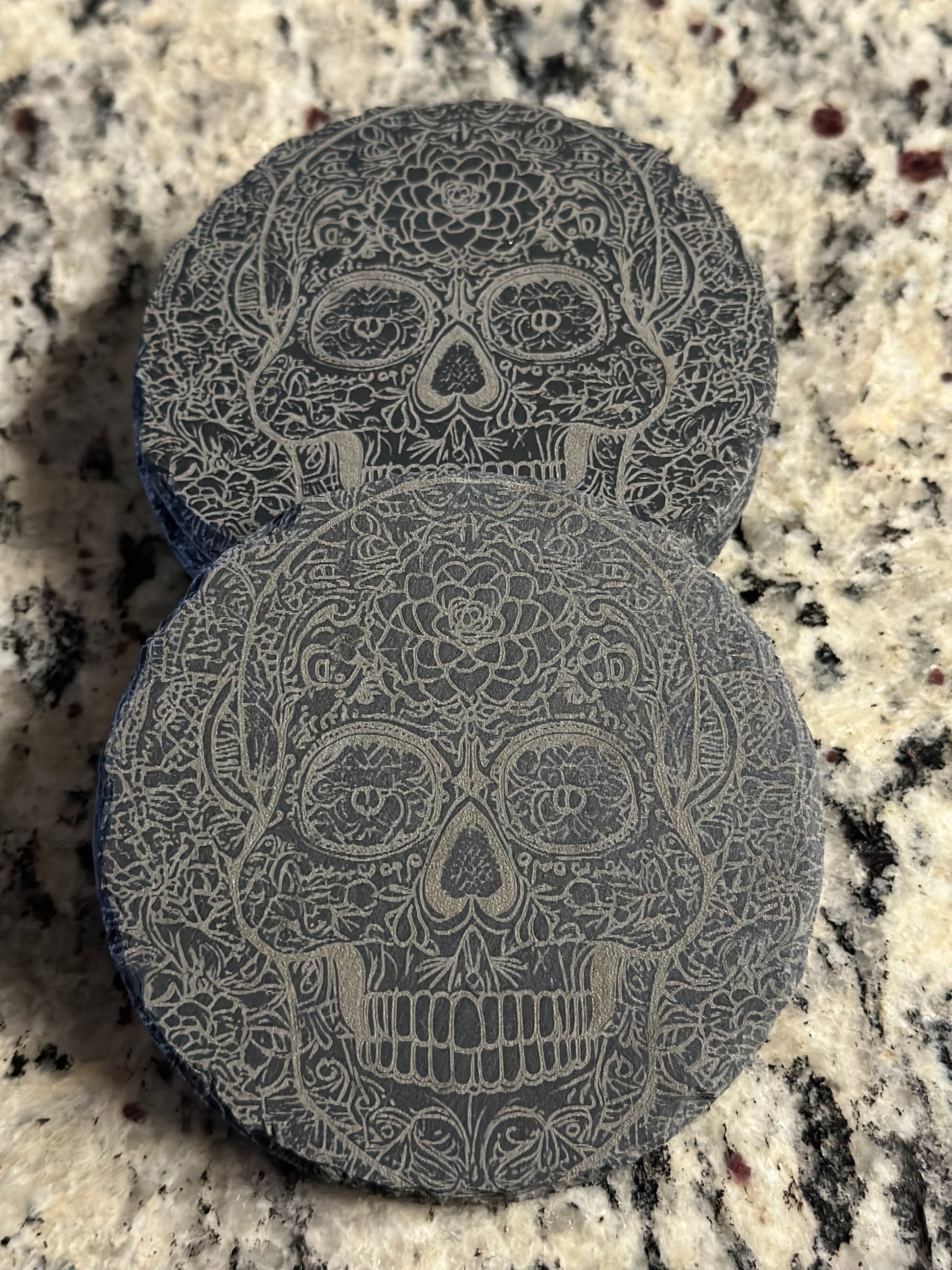A black slate coaster with an engraved pattern of Calavera.