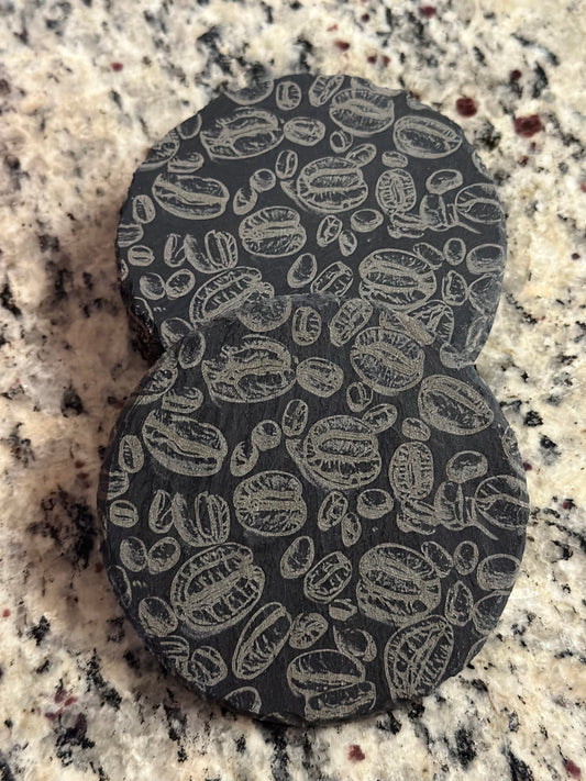 A black slate coaster with an engraved pattern of coffee beans.