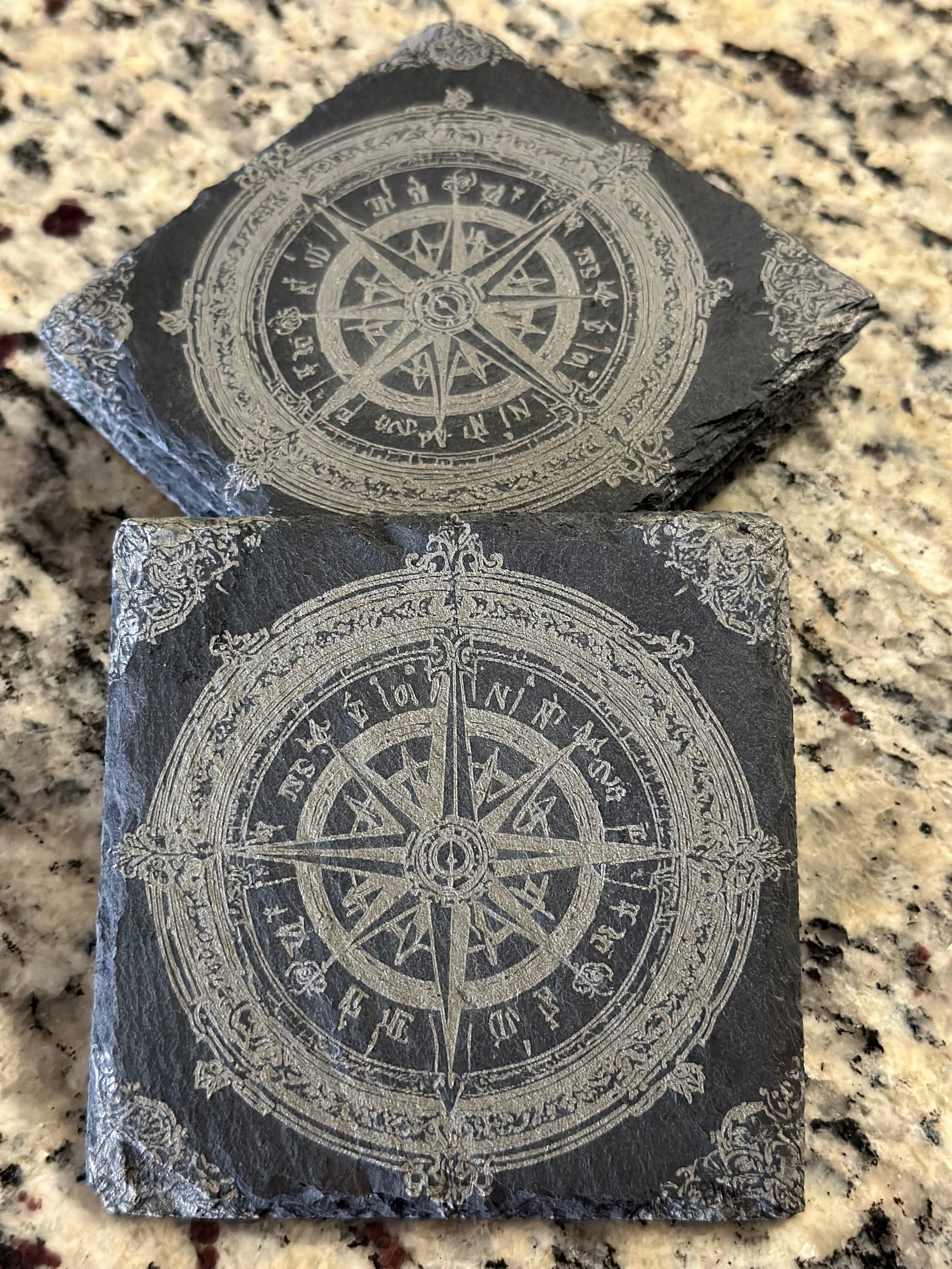 Engraved slate coasters with detailed map style compass on a dark slate background.