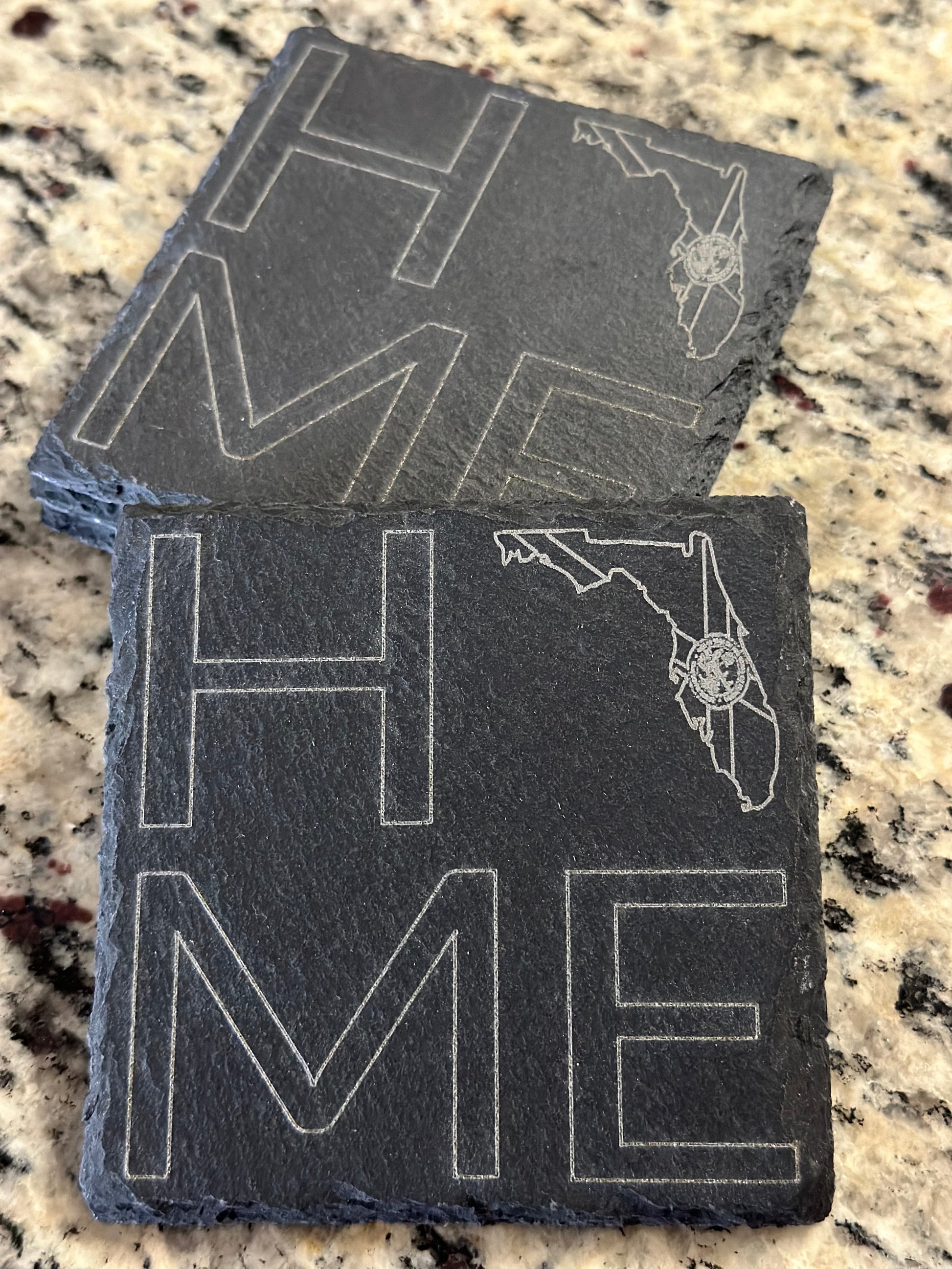 Engraved slate coasters with 'HOME' with FL State LOGO in place of O text on a dark slate background.