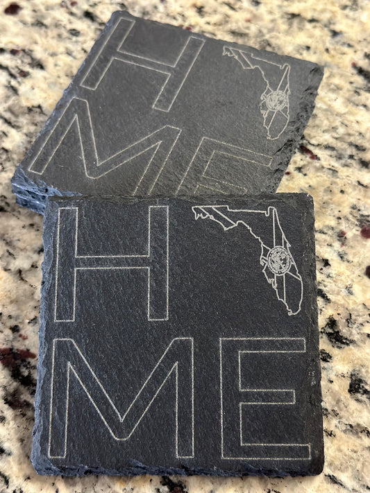 Engraved slate coasters with 'HOME' with FL State LOGO in place of O text on a dark slate background.