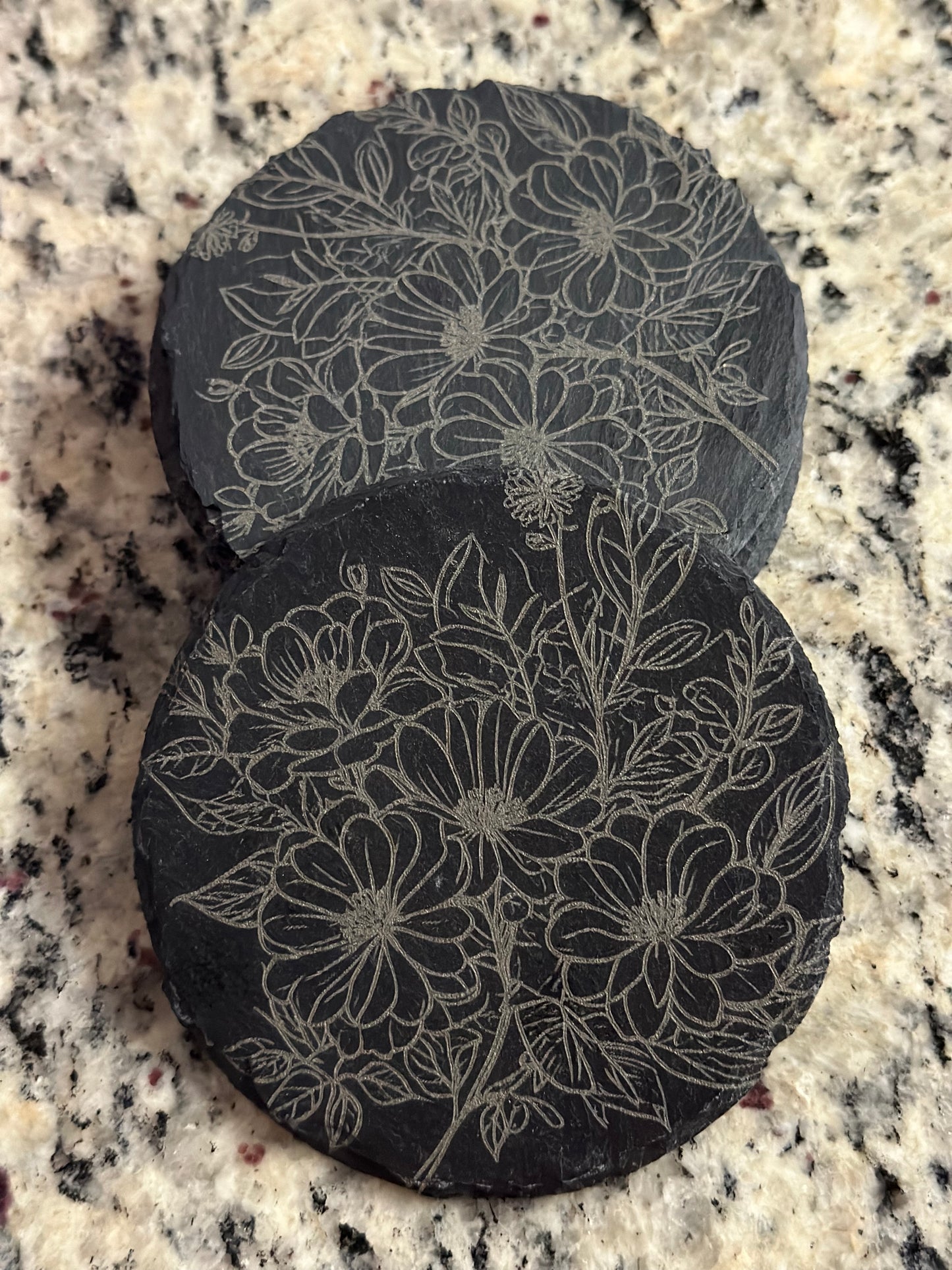 A black slate coaster with an engraved pattern of flowers.