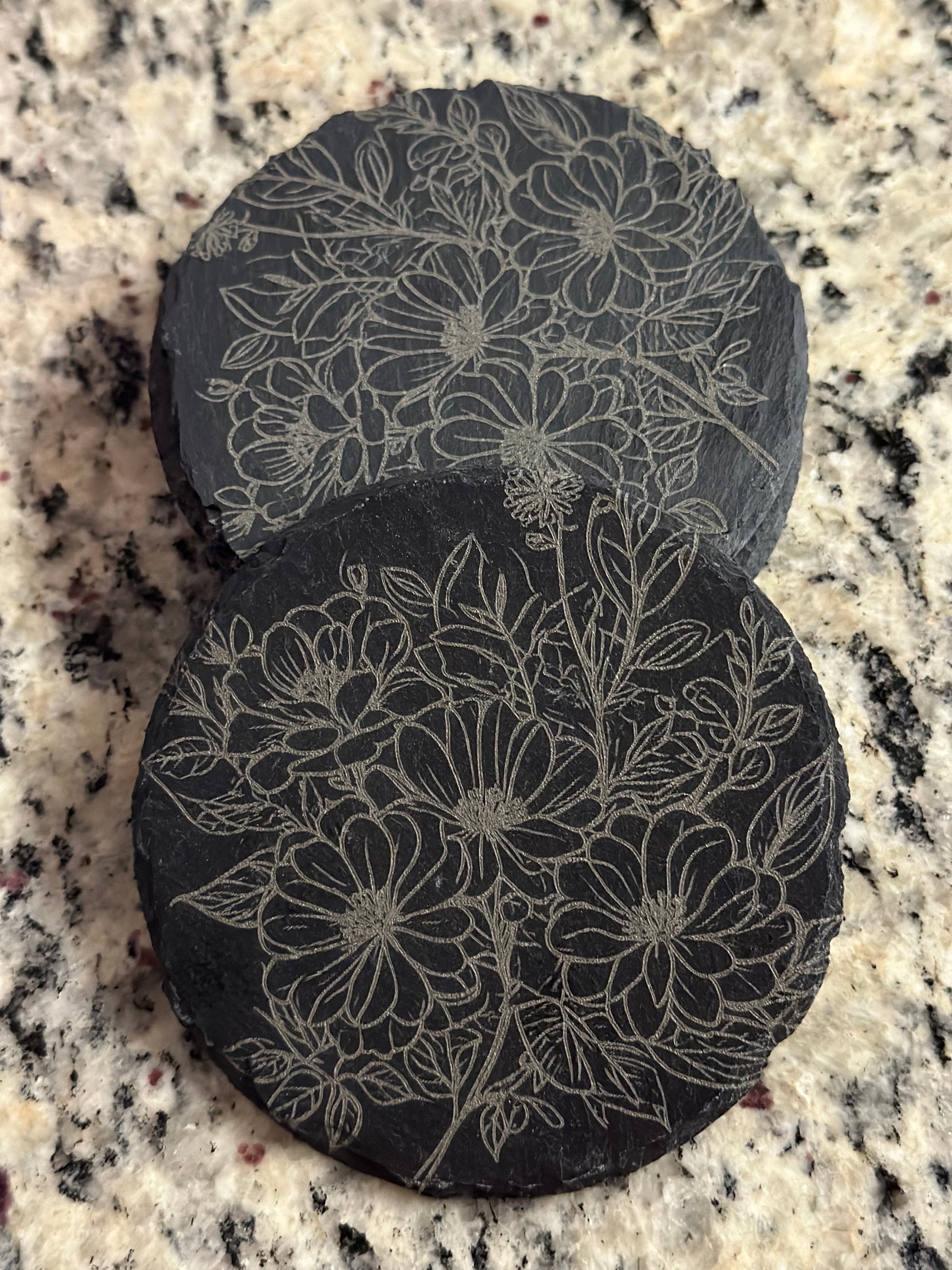 A black slate coaster with an engraved pattern of flowers.