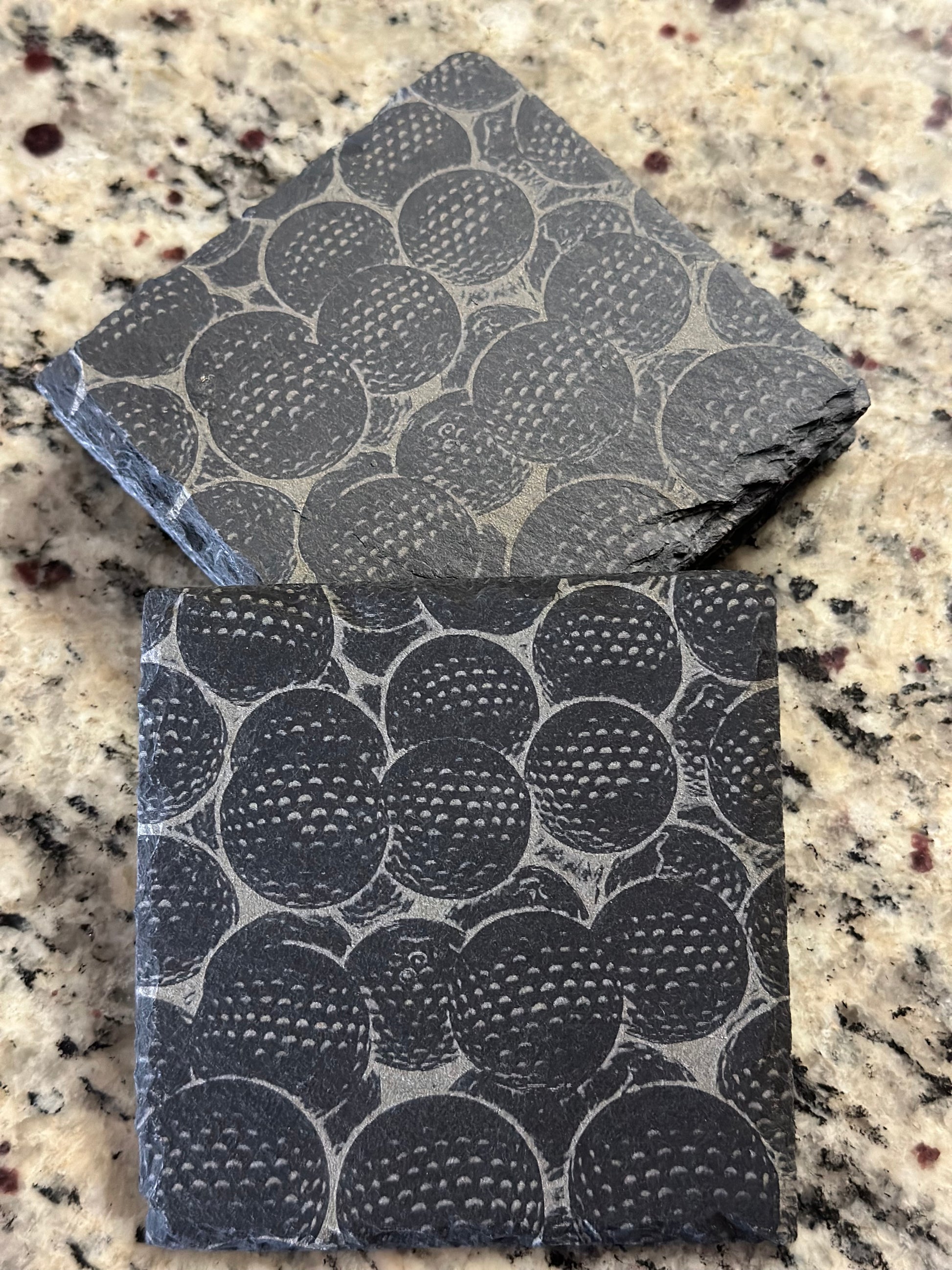 Engraved slate coasters with many golf balls on a dark slate background.