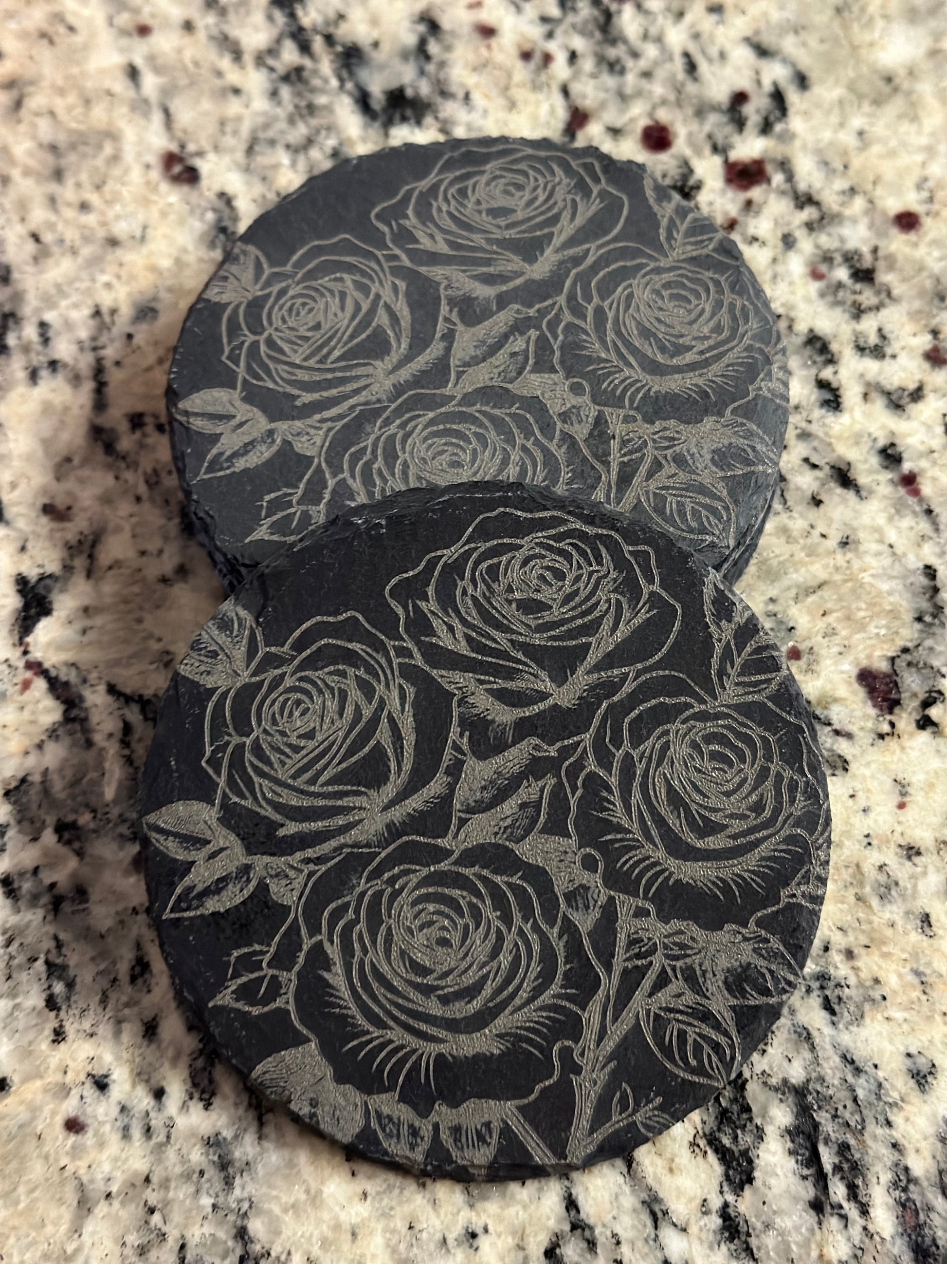A black slate coaster with an engraved pattern of roses.