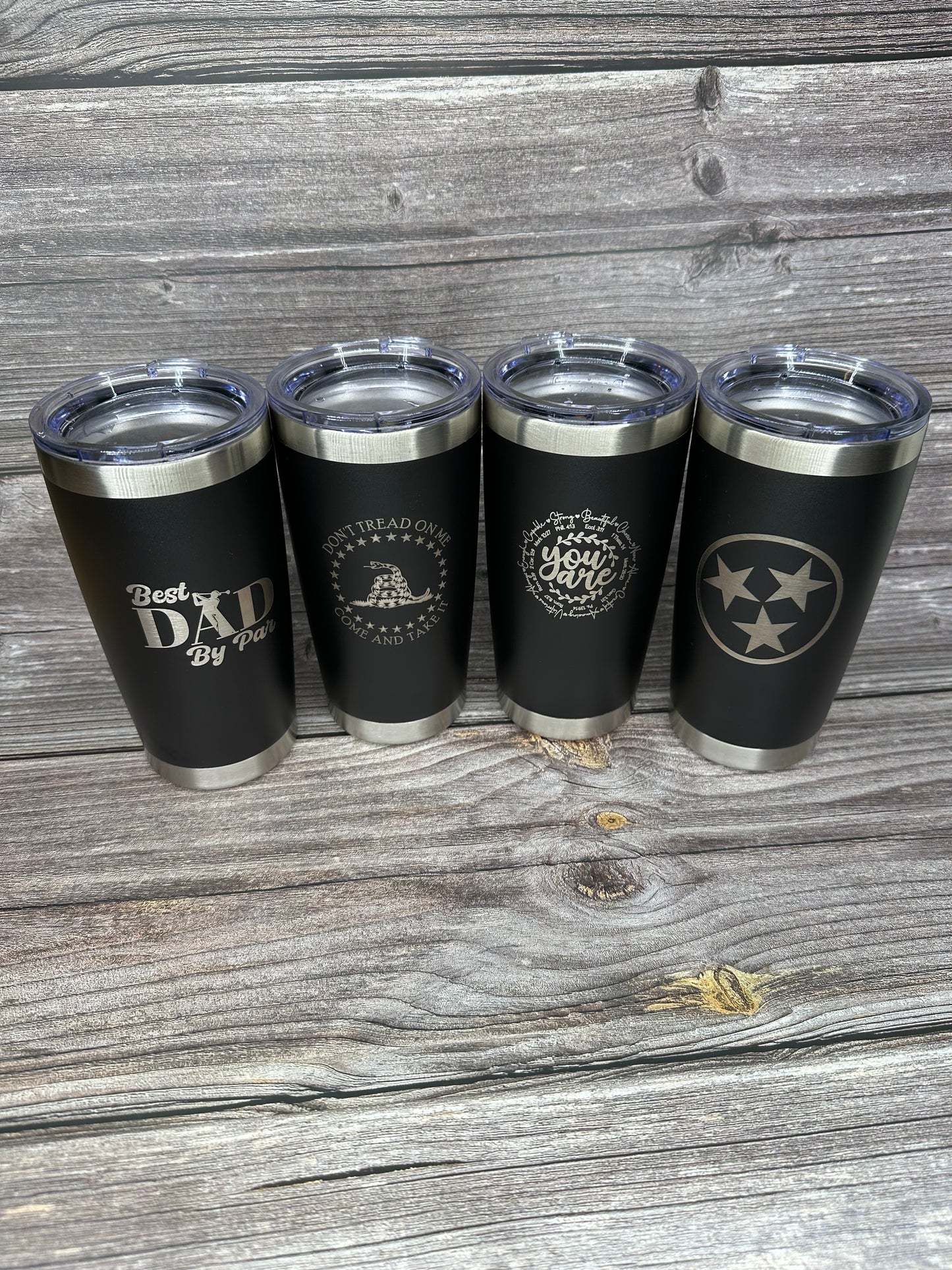 A set of four black 20oz laser engraved stainless steel tumblers with different designs.