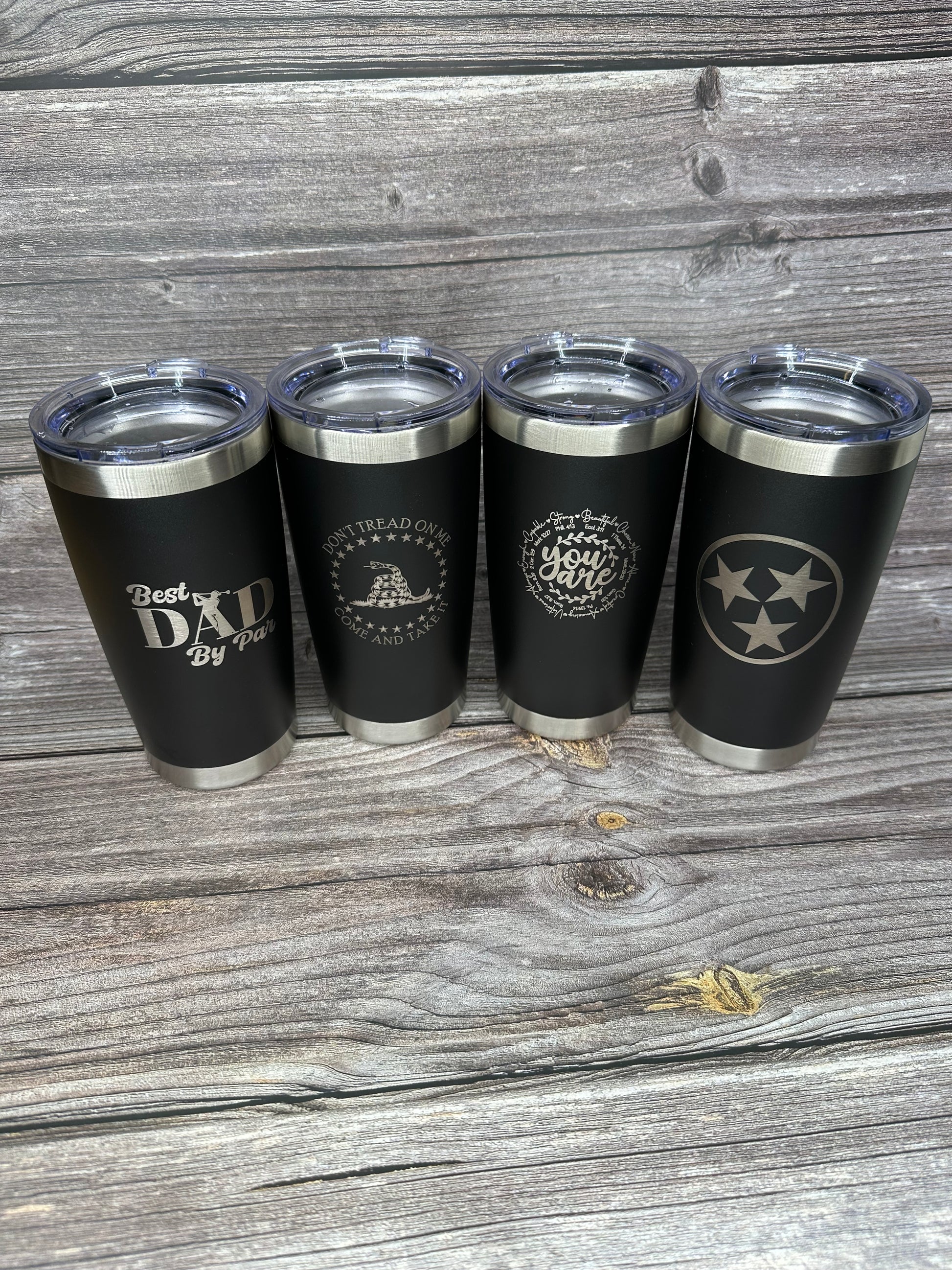 A set of four black 20oz laser engraved stainless steel tumblers with different designs.