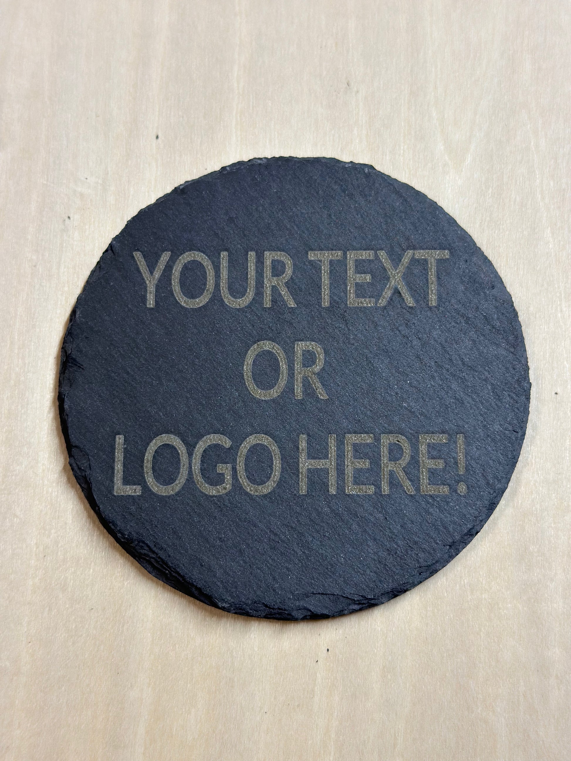 A round slate coaster with Your Text Or Logo Here! Placeholder text. 