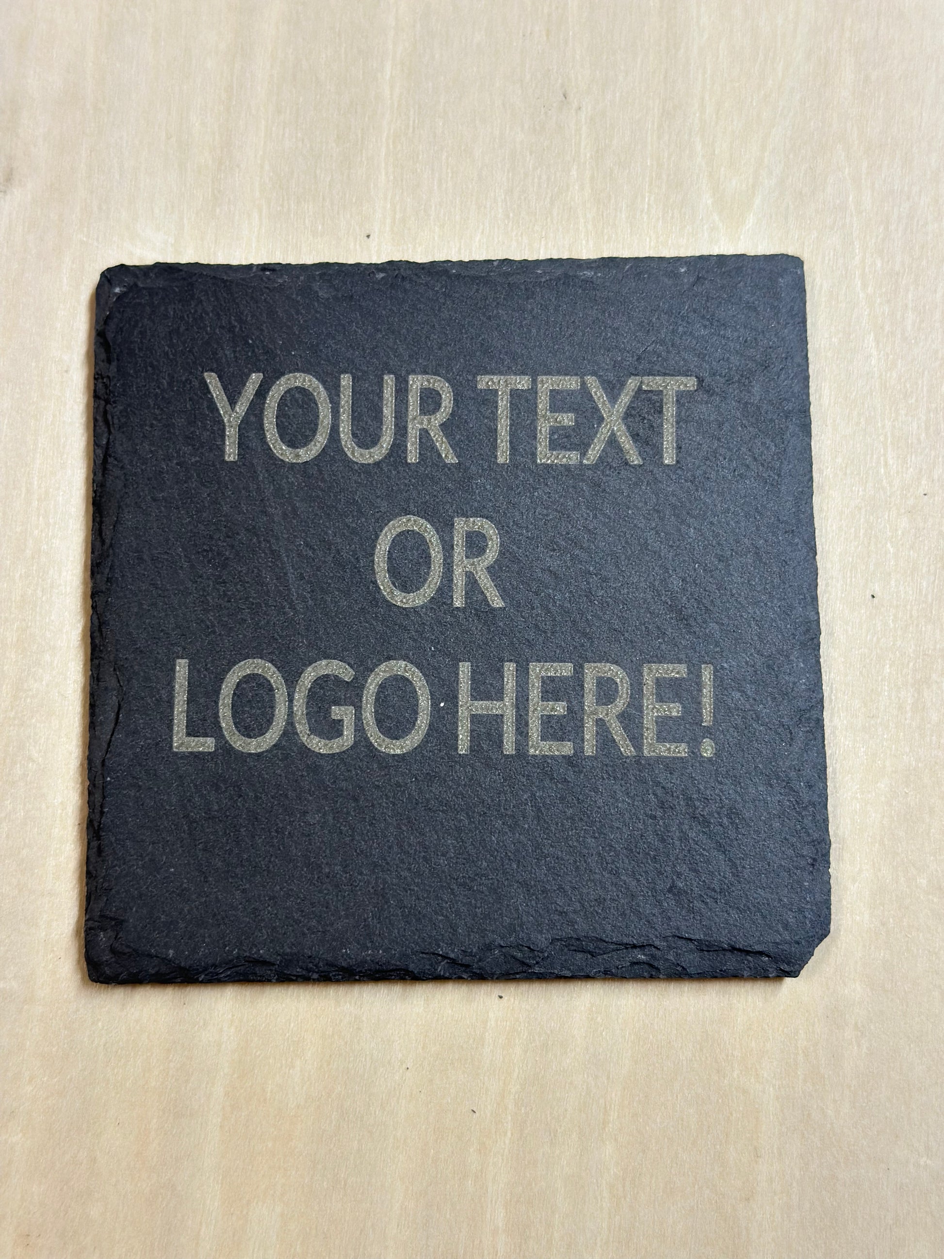 A square slate coaster with Your Text Or Logo Here! Placeholder text. 